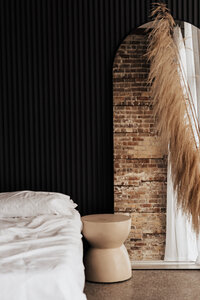 Detail shot of Tampa boudoir studio featuring white bedding, black panel wall, exposed brick, and pampas grass. Warm and moody interior designed for intimate photo sessions.
