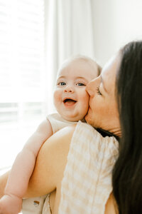 A close up picture of a mother kidding her baby son's cheek during an in home photography session in Wilmington, North Carolina