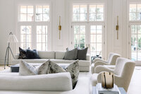 Interior Designer designed living room with white sofas, textured pillows, armchairs, tall windows, and soft natural light creating a calm, inviting mood.