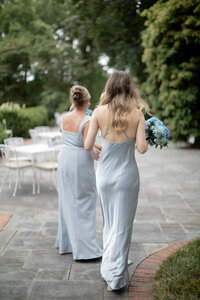 Bridesmaids in dusty blue satin gowns walk together carrying hydrangea bouquets