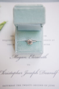 Diamond engagement ring displayed in a velvet box resting on a calligraphy wedding invitation