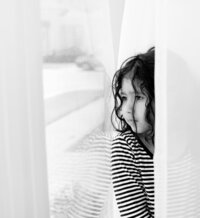 Candid black and white photo of a child by a window