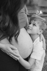 A son gazes up at his mother while holding her pregnant belly during her maternity photos in houston texas