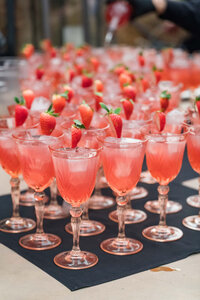 Rows of pink signature cocktails garnished with fresh strawberries for a wedding or special event.