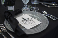 Black corporate event table setting with glass charger, menu, black linens and formal place setting in Phoenix Arizona