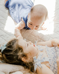A toddler girl and her baby brother laying on the floor smiling during an in home family photography session in Wilmington, North Carolina