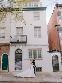 Bride and groom walk past a historic Philadelphia rowhouse with a flowing veil trailing behind