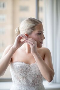 Bride puts on her earring in soft window light while getting ready