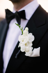 Close-up of a white freesia boutonniere pinned to the groom's black tuxedo lapel