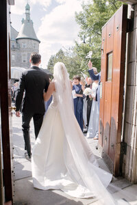 Bride and groom walk out through open church doors as guests cheer and wave ribbon wands