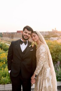 Radiant bride in long-sleeve white gown holds ivory bouquet on brick chapel steps adorned with holiday wreaths
