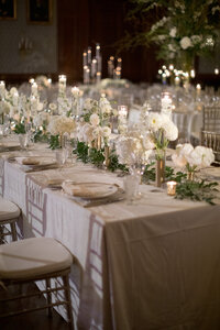 Long reception table set with white floral arrangements and candlelight beneath gilded portraits