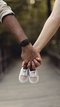 couple pregnancy announcement holding hands and baby shoes