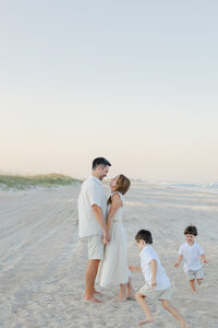 A mom, dad, and two toddler boys playing and laughing on the beach during their sunset family photography session at Wrightsville Beach, North Carolina