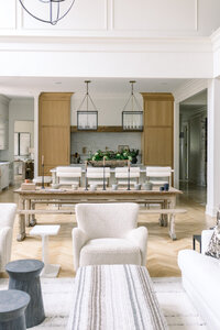 Professionally designed open-plan dining room with a long wood table, upholstered chairs, pendant lights, kitchen island, and neutral décor in a serene home.