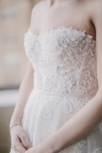 Close-up of a strapless wedding dress bodice with textured lace and a blush ribbon belt