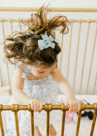 A toddler girl smiling and climbing into her crib during an in home family photography session in Wilmington, North Carolina
