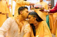Groom kisses turmeric-covered bride during a vibrant Indian haldi ceremony surrounded by family in yellow attire