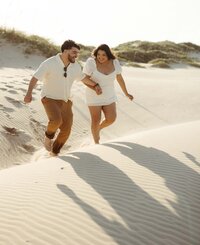 Couple running hand in hand through white sand dunes during an engagement session by Angie Rich Photography, a San Antonio photographer.