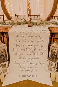 bride and groom's sweetheart table deocrated with a banner featuring their favorite bible passage from Corinthians