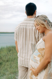 A couple walking along the beach with their dog in the backdrop during their maternity photography session at Wrightsville Beach, North Carolina