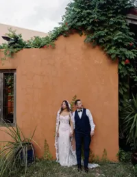 Bride and groom standing hand in hand in front of a vibrant orange stucco wall during romantic wedding portraits at Chapel Dulcinea wedding venue.