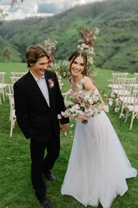 Bride and groom smiling with a floral bouquet at a romantic mountain destination wedding ceremony.