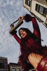 Human with red outfit holding up leopard print bag with cloudy blue sky in the background