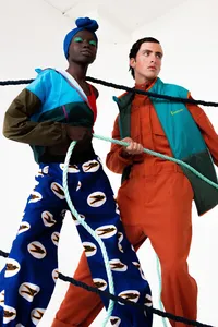Two humans, one in blue patterned pants and the other in an orange outfit with a puffy blue vest