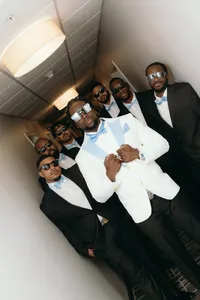 Groom and groomsmen standing with sunglasses on, with groom in white tux and groomsmen in black tuxes
