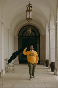 Human standing in yellow university sweatshirt and walking outside in front of large pillars while holding black garment