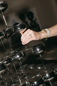 Hand with ring reaching to grasp a cocktail glass from tower of glasses