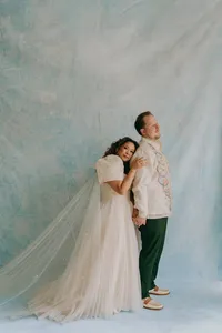 Powder blue and white backdrop with couple standing in front of it in formalwear, while one human hugs the other from behind