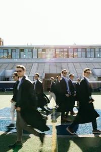 Nine humans dressed in formalwear and graduation gowns looking off in different directions at stadium