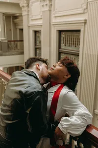 Two humans embracing and one kissing the side of the other's neck in a courthouse setting