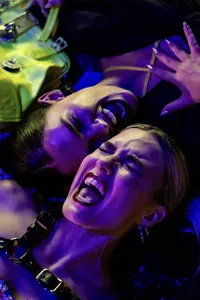 Two humans with mouths open, purple lighting and screaming with faces laying down and close to one another