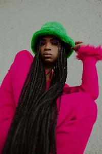 Human in hot pink outfit and bright green hat, looking down at the camera
