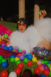 Human looking at camera with white fluffy outfit and muti-color balls surrounding them