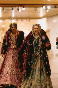 Two humans holding hands and wearing beautiful headwear, dresses and jewelry with big smiles at their celebration of love