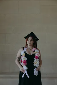 Human with beautiful blooming floral sash and wearing black graduation cap, looking away from camera