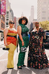 Three humans standing in the city street, looking at the camera with sunglasses and colorful outfits
