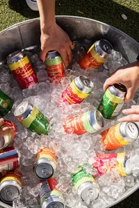 Close up of a multitude of Anytime flavors in ice with hands holding some of the cans