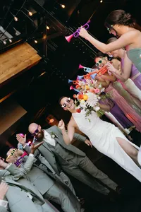 Couple walking out of their celebration of love with attendees blowing play trumpets and the couple has sunglasses on