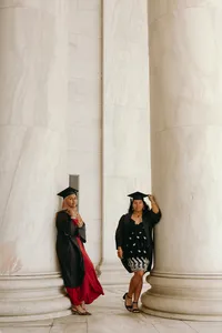 Two individuals, one in a red dress and one in a black dress, wearing graduation caps and looking at camera