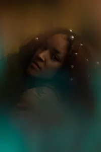 Dimly lit human looking at the camera with sparkles near their hair