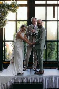 Couple exchanging vows with officiant standing nearby, while they hold hands and laugh