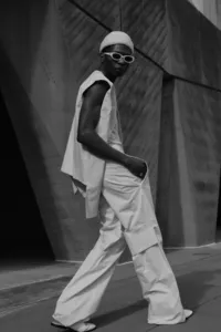 Black and white image of human walking in city street and looking at the camera with sunglasses on