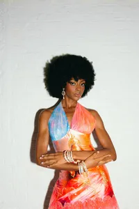 Individual looking at camera with beautiful pink, blue and orange halter outfit with silver bracelets