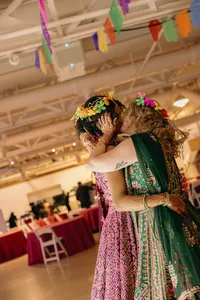 Two humans, in pink and green colorful dresses, kissing and holding one another at celebration of love