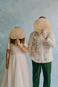 Powder blue and white background with couple standing in the foreground with fans covering their faces